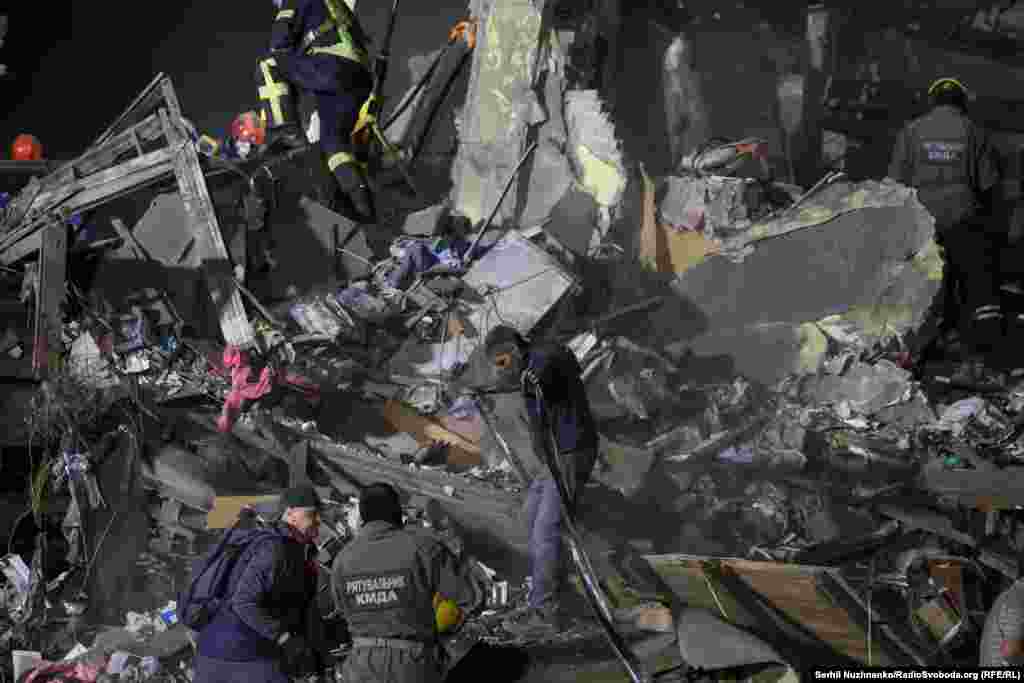 Спасатели работают на месте попадания российской баллистической ракеты в жилой дом в Киеве.Спасатели бросились вытаскивать выживших из-под завалов, прислушиваясь к звонкам мобильных телефонов, чтобы попытаться найти людей, оказавшихся под завалами