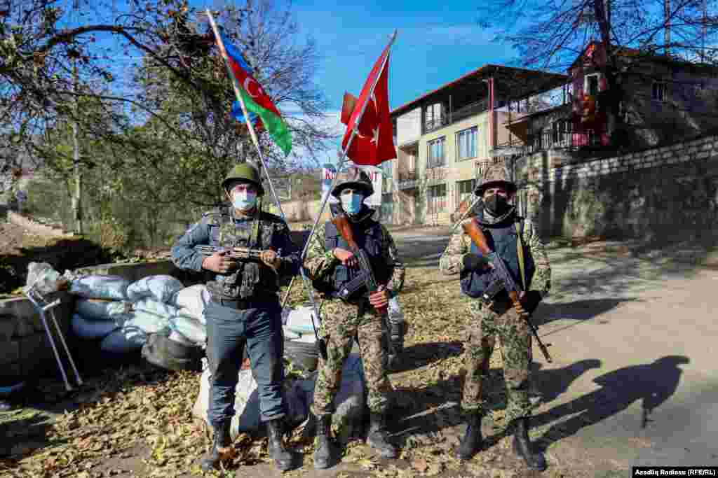Azerbaijani servicemen stand guard before Azerbaijani and Turkish flags at a checkpoint in the Nagorno-Karabakh town of Hadrut on November 25, 2020. Azerbaijani prosecutors will investigate a video, widely distributed on social media, that allegedly showed Azerbaijani forces' earlier execution of two ethnic Armenian men in Hadrut, Azerbaijani President Ilham Aliyev's senior foreign-policy aide Hikmat Hajiyev told PBS Newshour, a U.S. TV news program, on November 30, 2020.&nbsp;