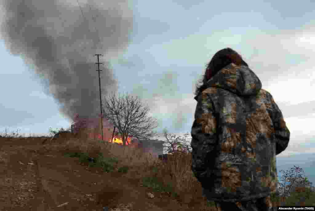A local resident watches a burning house in the town of Lachin (Berdzor) on November 30, 2020, the day before the town returned to Azerbaijani control. Another town resident told Agence France Presse that he had no intention of leaving: "People live on both sides of borders after wars, and things are fine," said the man, a grocery-store owner.&nbsp;